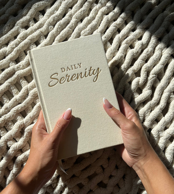 Daily Serenity journal being held between a womens two hands with natural sunlight 