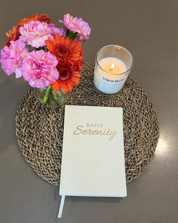 Notebook titled 'Daily Serenity' with a lit candle and flowers on a textured surface