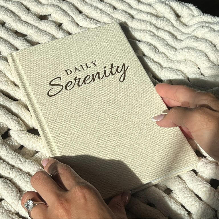 Daily Serenity sobriety journal being held in between a womens two hands in natural sunlight 
